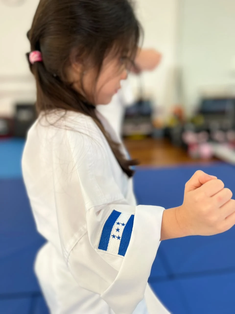 Alumna de Okami Dojo practicando karate con la bandera de Honduras en su uniforme